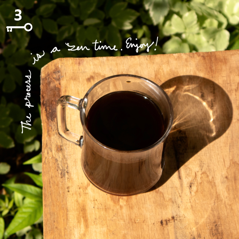 A glass of rich black coffee sitting on a wood table outside with sunlight and shadow, and the text overlay reads, “The process is a zen time … Enjoy!”